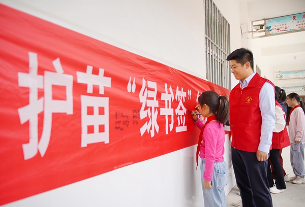 塔山镇中心小学学生和志愿者一起在护苗“绿书签”宣传活动横幅上签名。刘冰摄